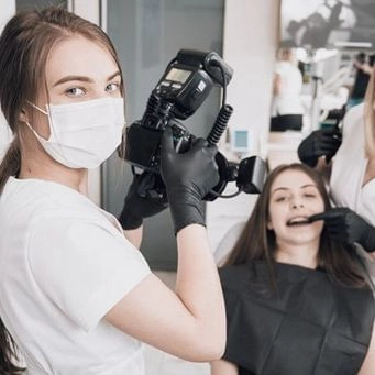 Dental assistant photographing patient's teeth with a camera and flash.