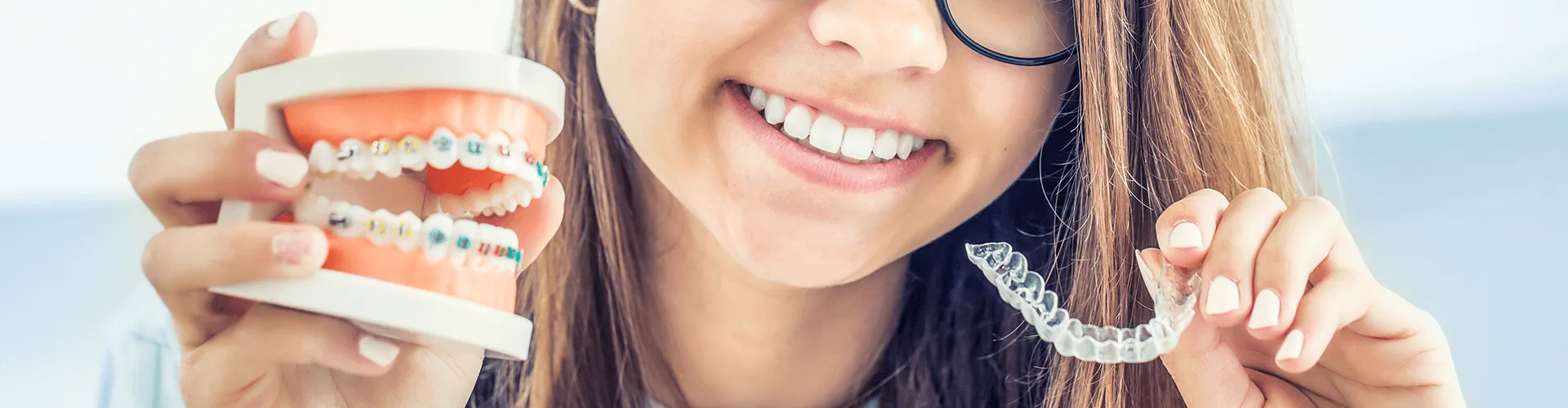 teen holding braces model and clear aligner