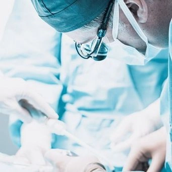 Surgeon performing a surgical procedure, wearing surgical mask and loupes.