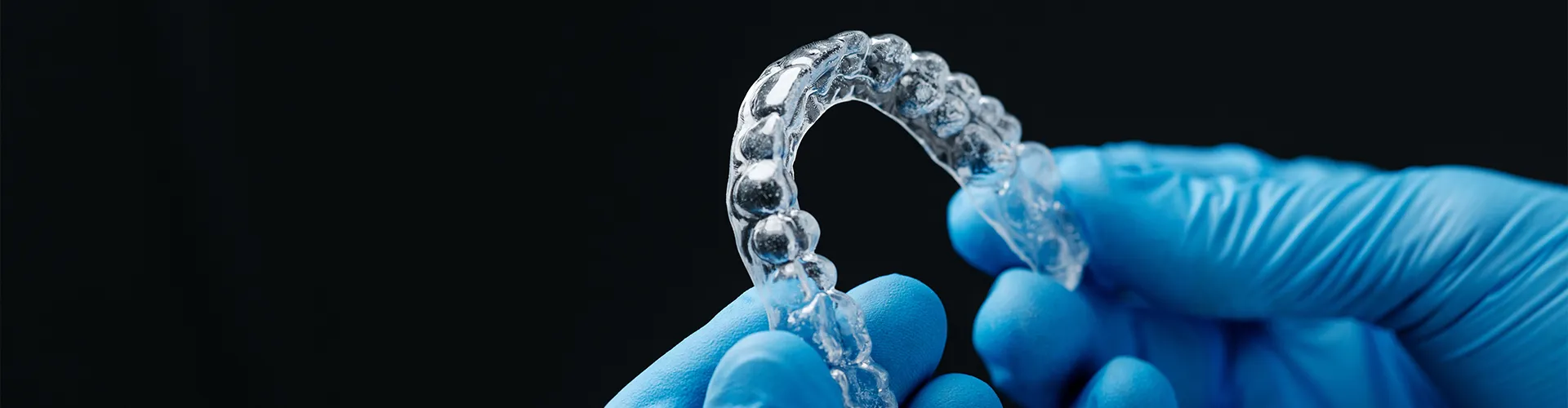gloved hands holding a clear aligner